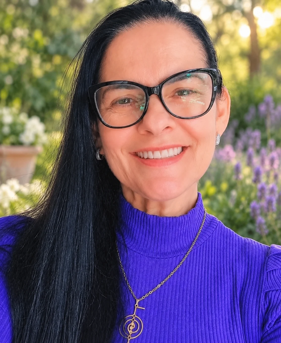 Retrato da terapeuta sorrindo, de óculos e blusa violeta, em um jardim florido.
